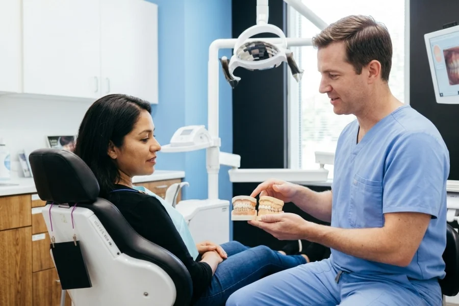 Dentista comparando un onlay dental y una corona dental durante una consulta